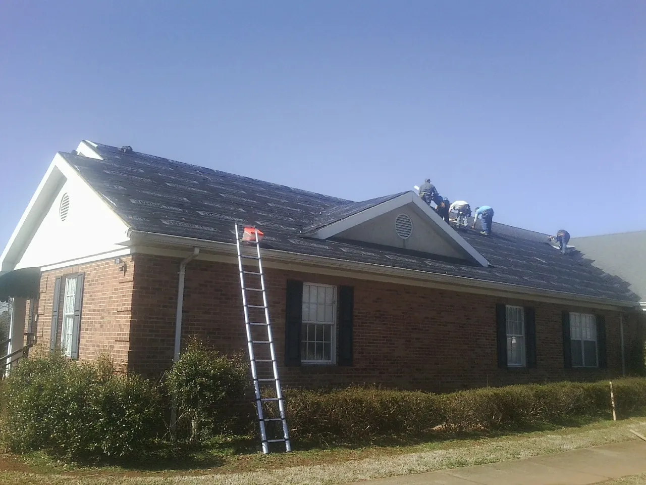 Crew tearing shingles off a brick ranch roof with a ladder set — Metal Roof Repair work by our crew in Geuda Springs