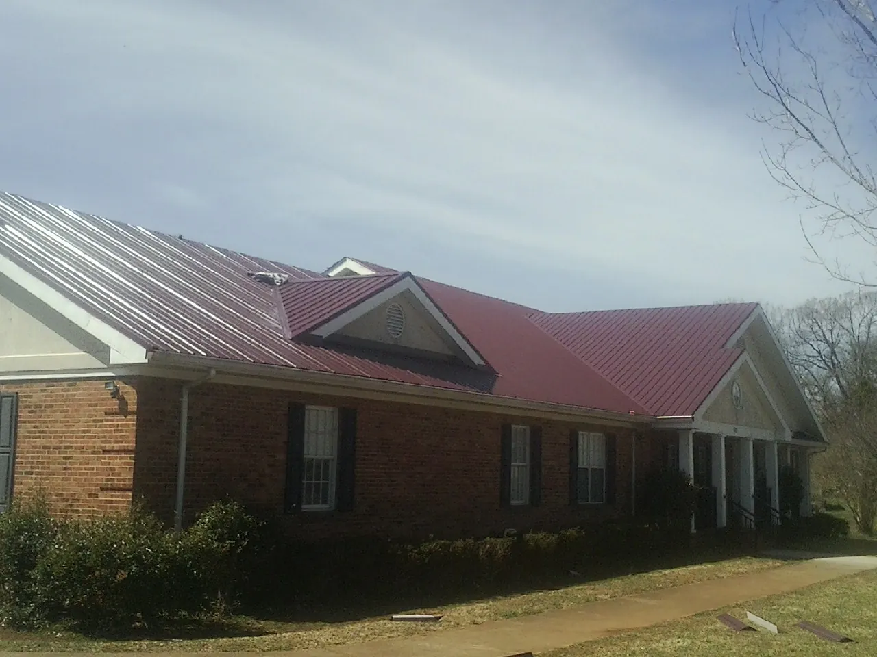 Red metal roof with gabled entries on a long brick building, from a Hail Damage Roof Repair job in Geuda Springs