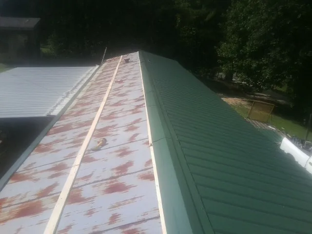Old rusted panels beside newly installed green metal roofing — Wind Damage Roof Repair by Roofing Brothers in Geuda Springs