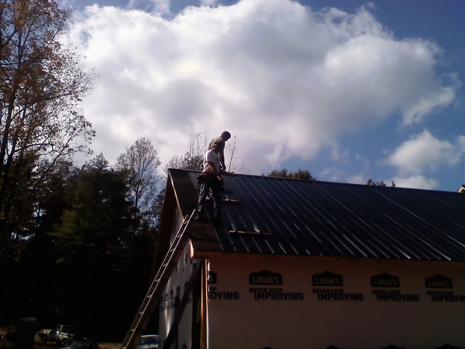 Roofer fastening dark metal panels high against a cloudy sky, from a Roof Inspection job in Geuda Springs