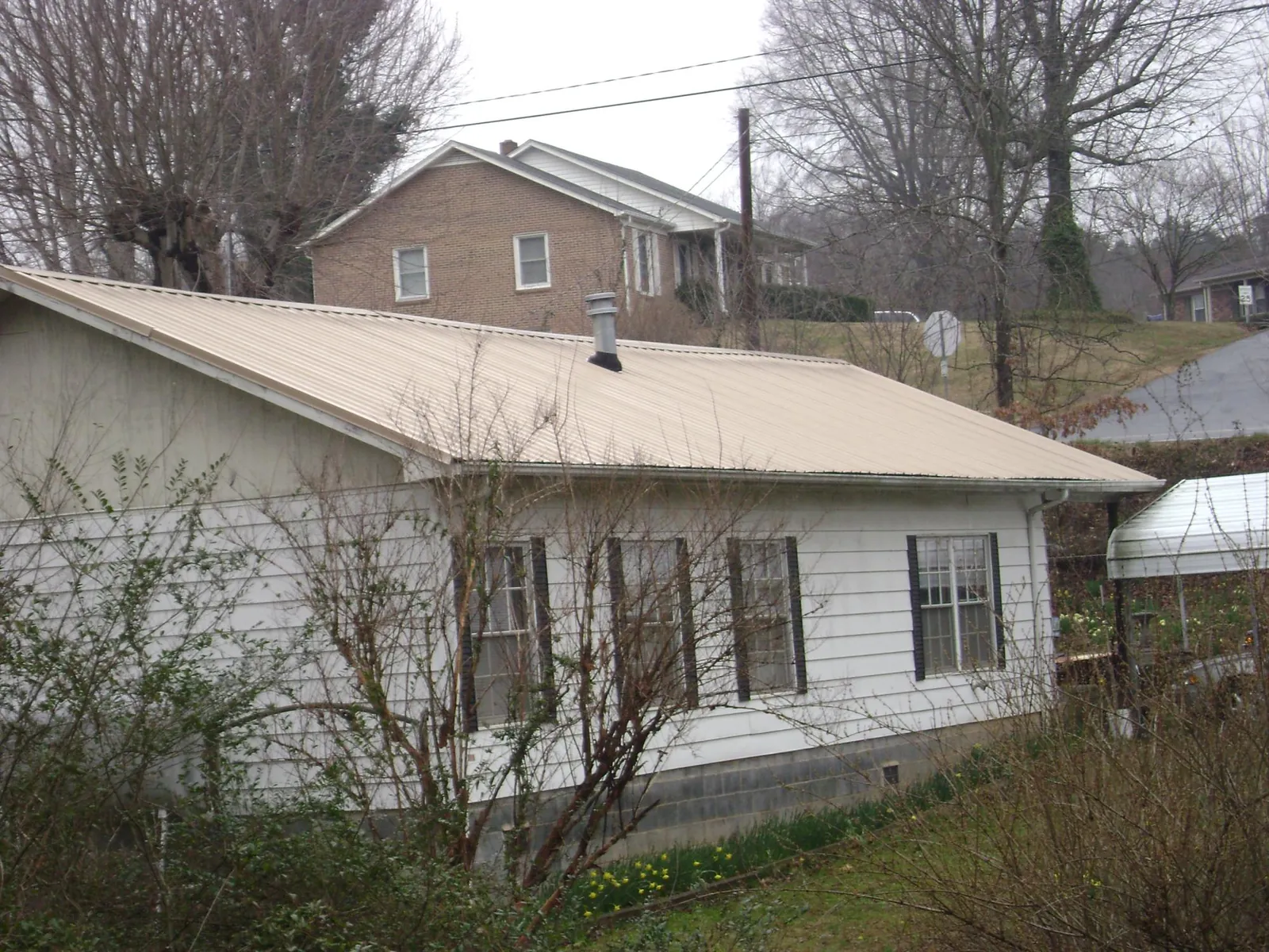 Tan metal roof on a white sided house set into a hillside — Commercial Roofing by Roofing Brothers in Geuda Springs