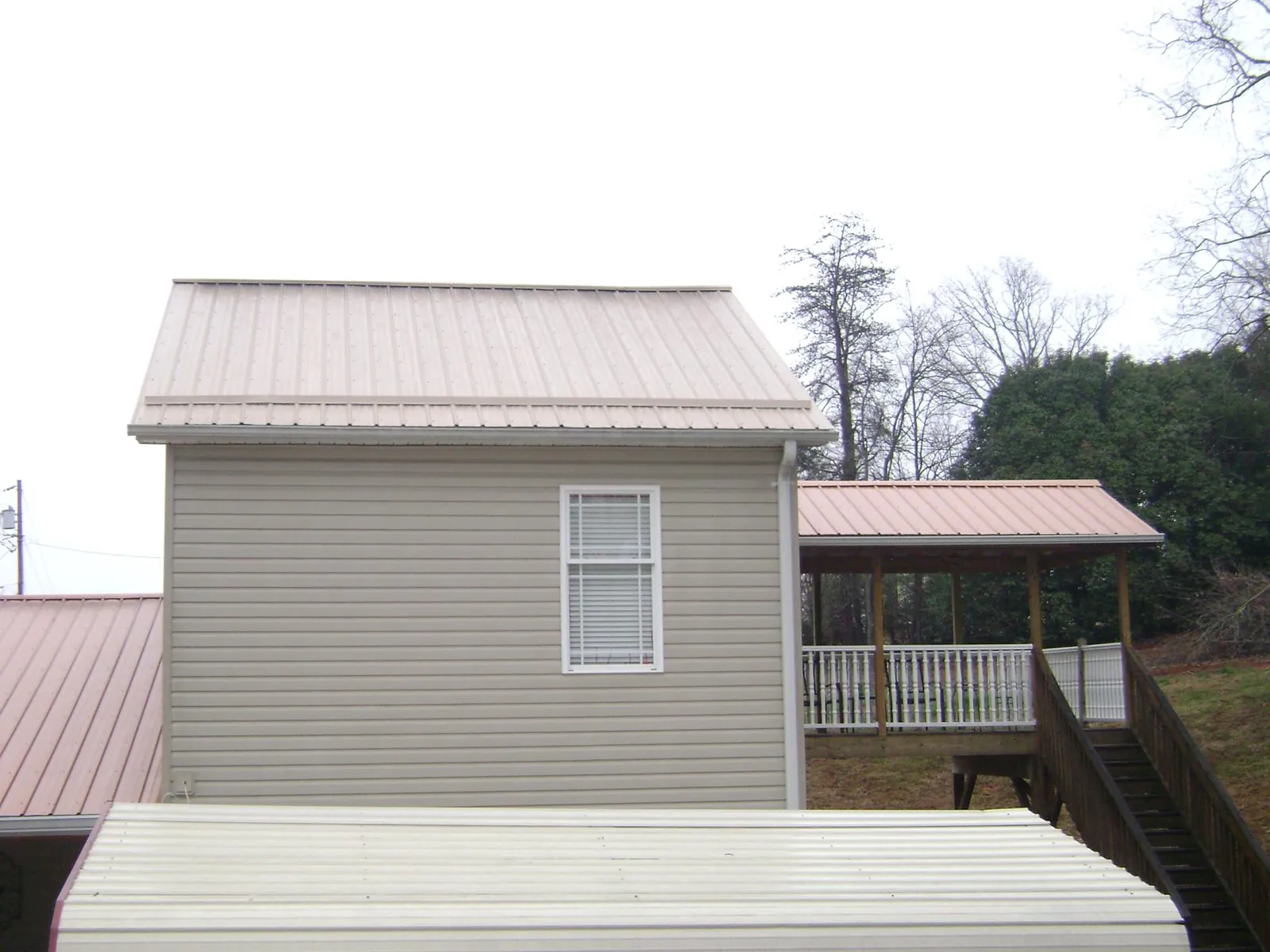 Tan metal roofs on a two story addition and attached porch, from a Roof Replacement job in Geuda Springs